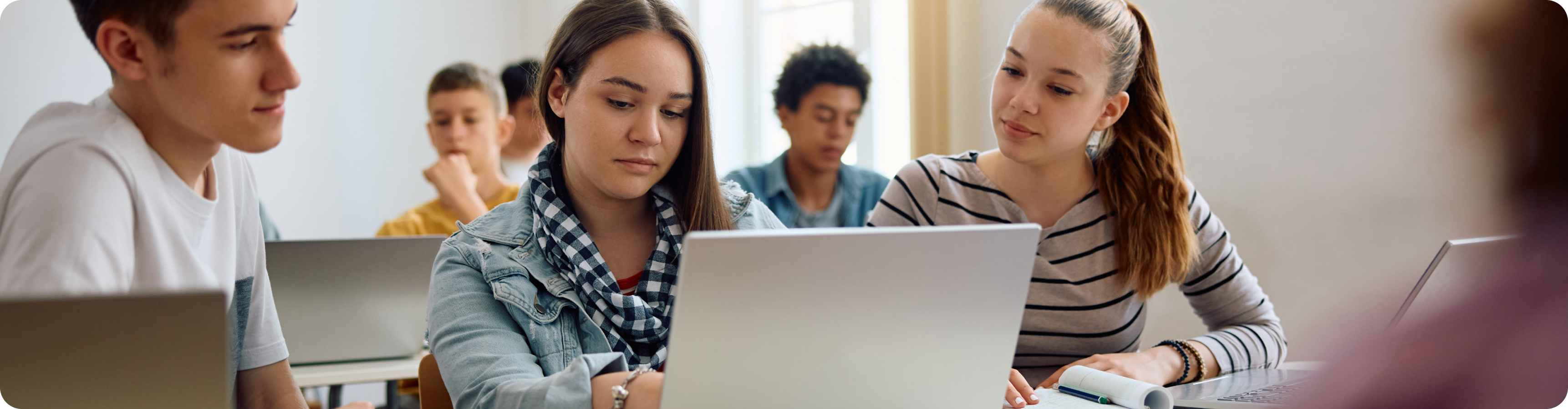 3 Students sitting together in classroom looking in same Laptop